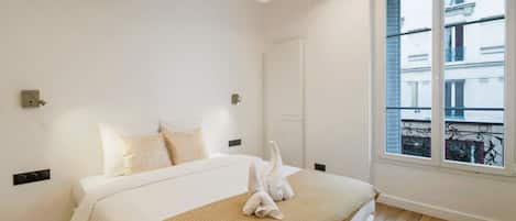 A bedroom with a bed, a window, and a view of buildings outside.