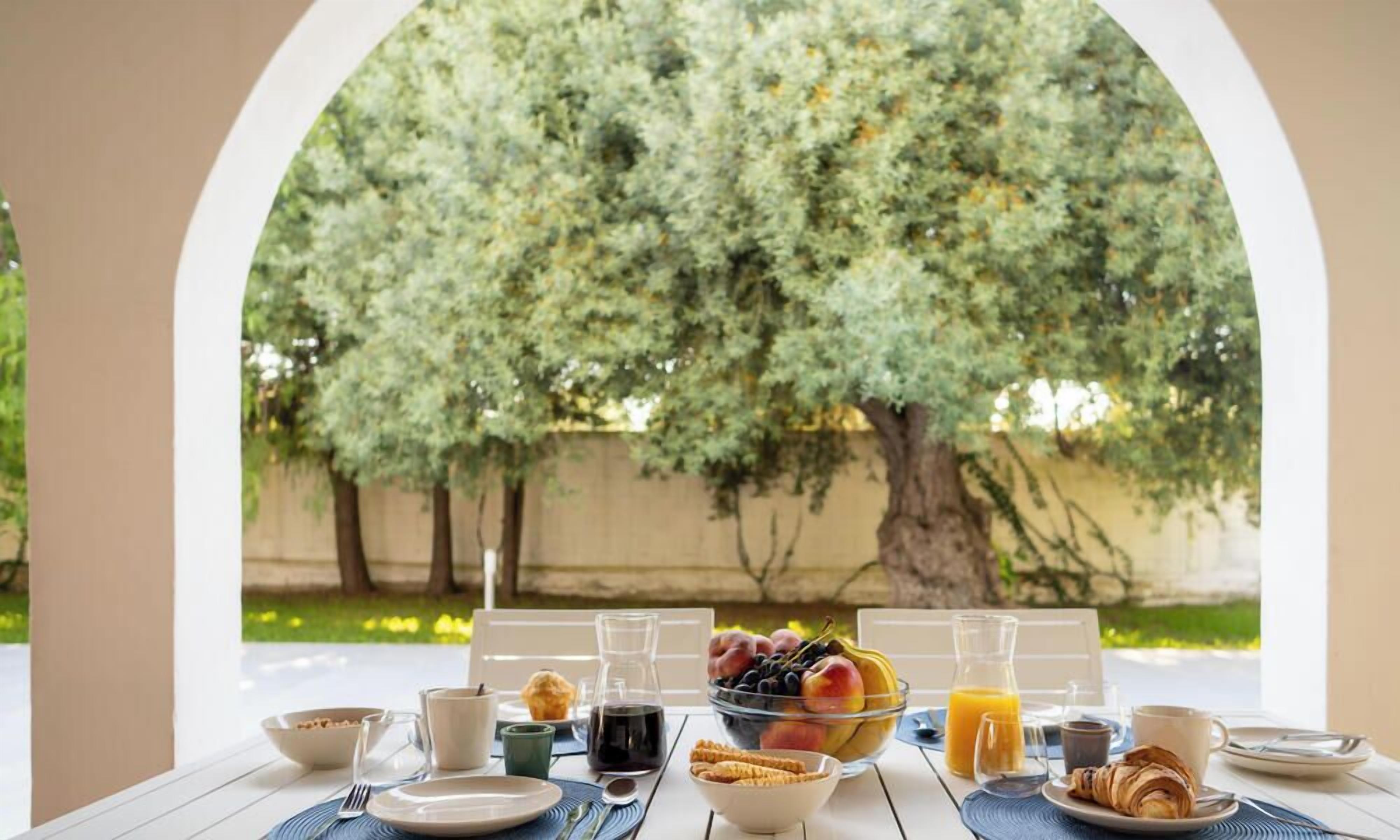 An outdoor breakfast setting with a table, breakfast items, and a view of trees.