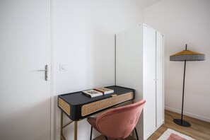 Ein kleiner Raum mit Schreibtisch, Stuhl und einer Stehlampe.