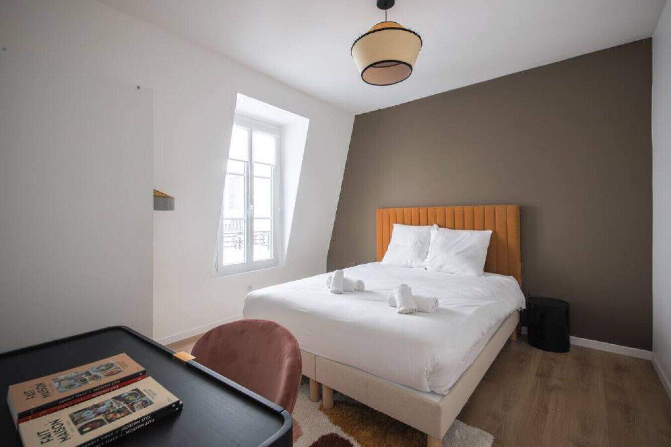 Ein Hotelzimmer mit Bett, Schreibtisch, Stuhl, Fenster und Deckenlampe.
