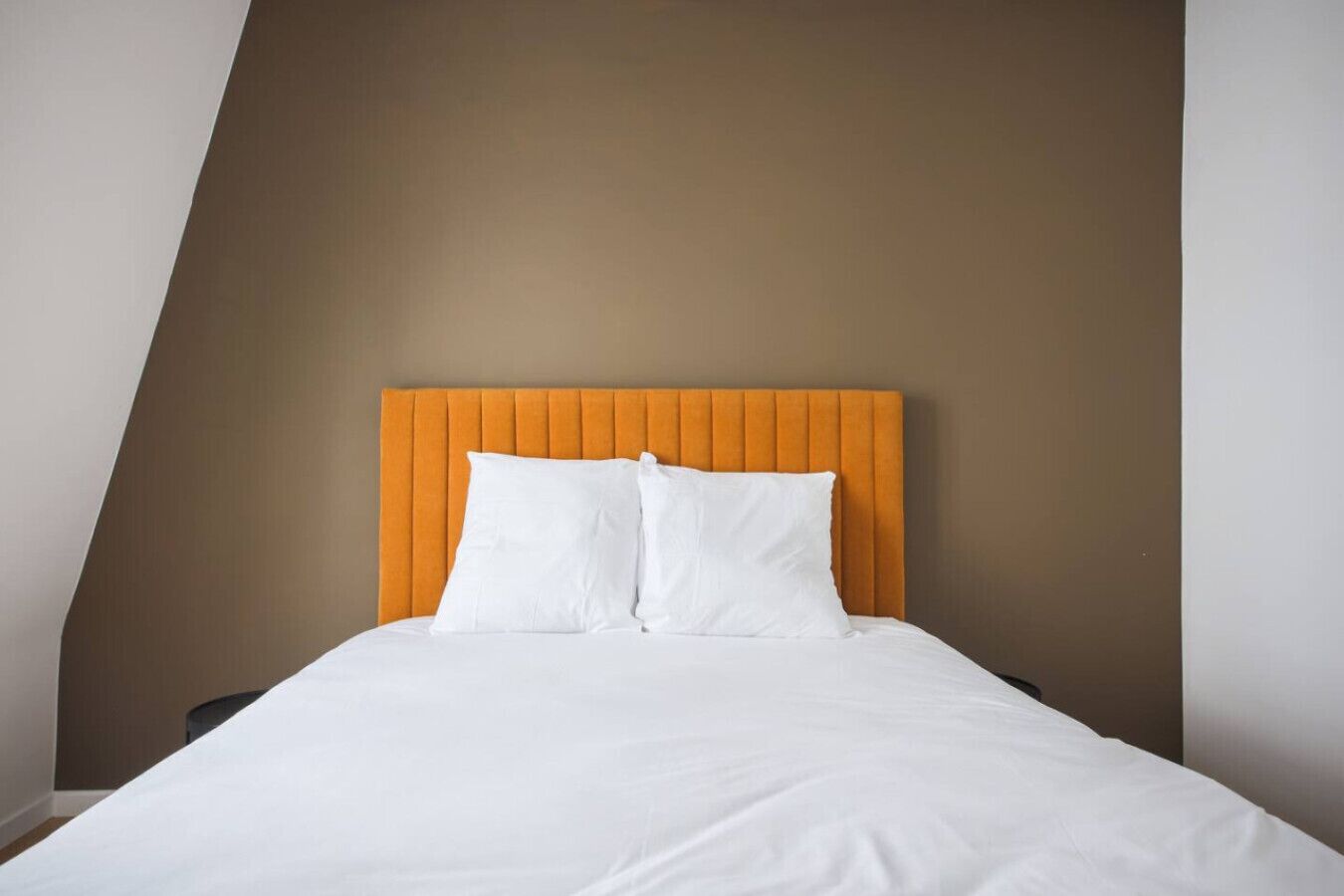 A bed with a headboard, white bedding, and a brown wall.
