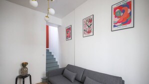 Een moderne woonkamer met een grijze bank, een klein tafeltje met een vaas, en een trap naar een hoger niveau.