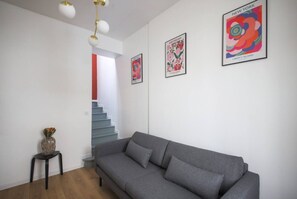Ein modernes Wohnzimmer mit einem grauen Sofa, einem kleinen Tisch mit einer Vase und einer Treppe, die zu einer weiteren Ebene führt.