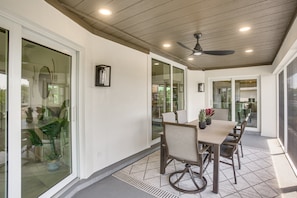Ein überdachter Patio-Bereich mit Esstisch, Stühlen, Deckenventilator und Topfpflanzen.