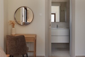 Une pièce comprenant un bureau en bois, une chaise, un miroir et une salle de bain avec un lavabo et un miroir.