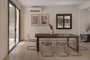 A dining area with a wooden table and clear chairs, a vase with dried plants, and two framed artworks on the wall. - Phaedrus Living: Luxury Villa Green Bay (Paralimni)