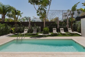 A rectangular swimming pool with a ladder, surrounded by lounge chairs and greenery. - Phaedrus Living: Luxury Villa Green Bay (Paralimni)