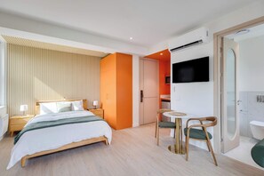 A modern hotel room with a bed, bedside tables, a TV, a small table with chairs, and a bathroom with a toilet and shower. - 305 Cook - Loft in the Heart of Old Quebec (Québec)
