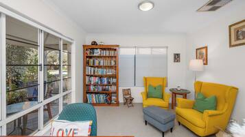 A cozy living room with a bookshelf, two yellow armchairs, a small table, and a window with a view.