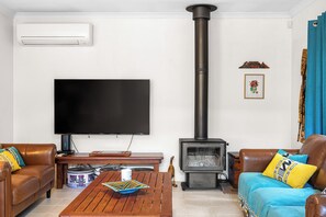 A living room with a flat-screen TV, a wood-burning stove, a coffee table with a decorative bowl, and two leather sofas with patterned cushions. - Riverside Retreat Near Curtin Uni & Lo Quay Café (Wilson)