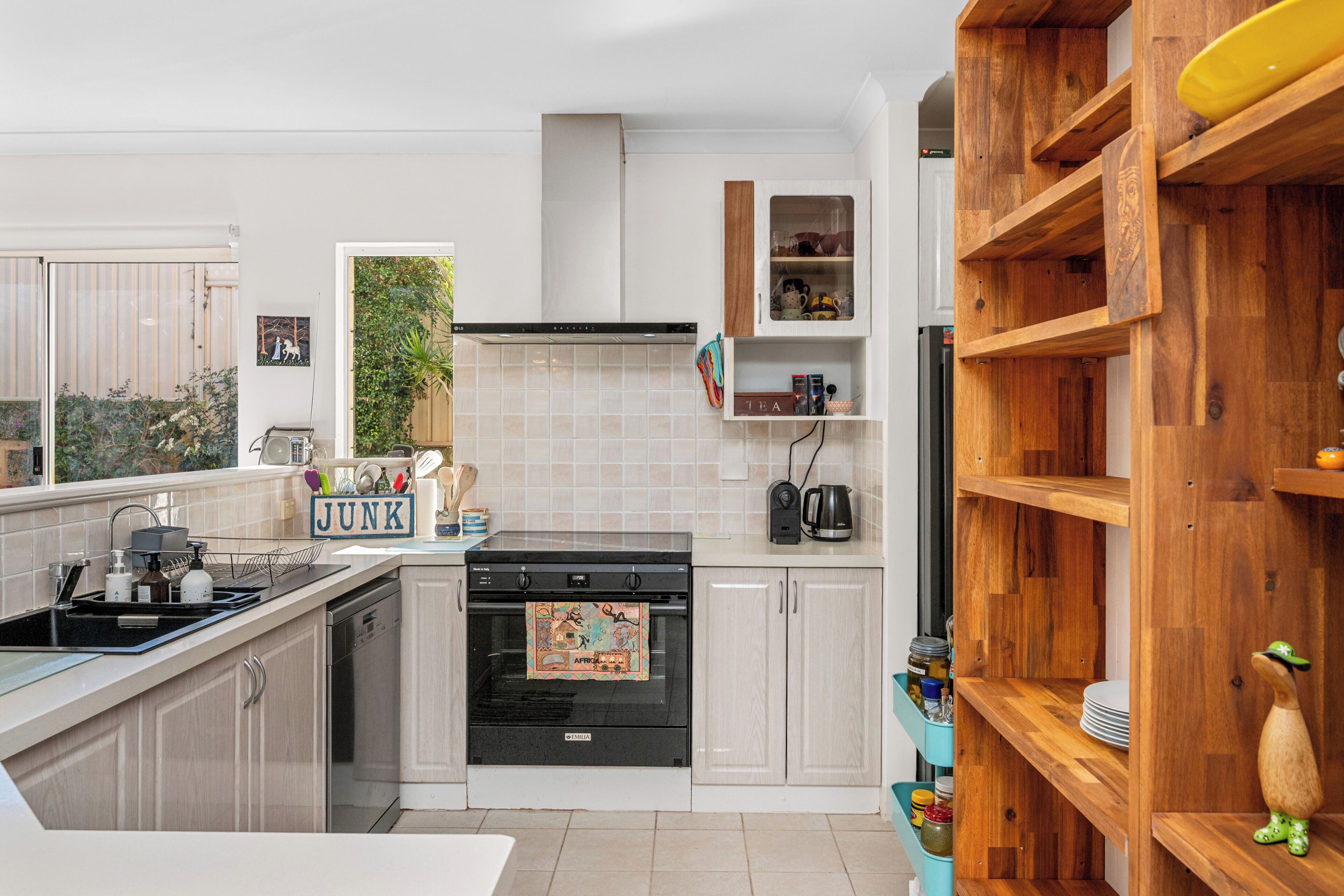 A modern kitchen with a stove, sink, and wooden shelving.
