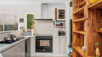 A modern kitchen with a stove, sink, and wooden shelving.