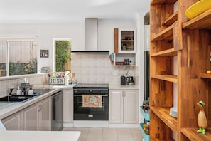 A modern kitchen with a stove, sink, and wooden shelving. - Riverside Retreat Near Curtin Uni & Lo Quay Café (Wilson)