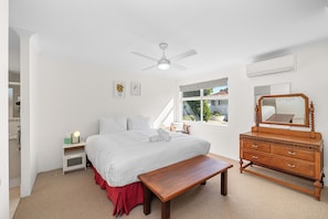 A bedroom with a bed, a wooden dresser, a bench, a ceiling fan, and a window with a view of the outside. - Riverside Retreat Near Curtin Uni & Lo Quay Café (Wilson)