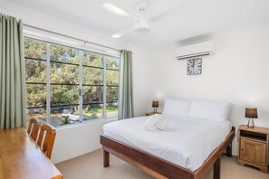Hotelkamer met een bed, twee nachtkastjes, een raam met gordijnen, een plafondventilator, een airconditioning en een wandklok.
