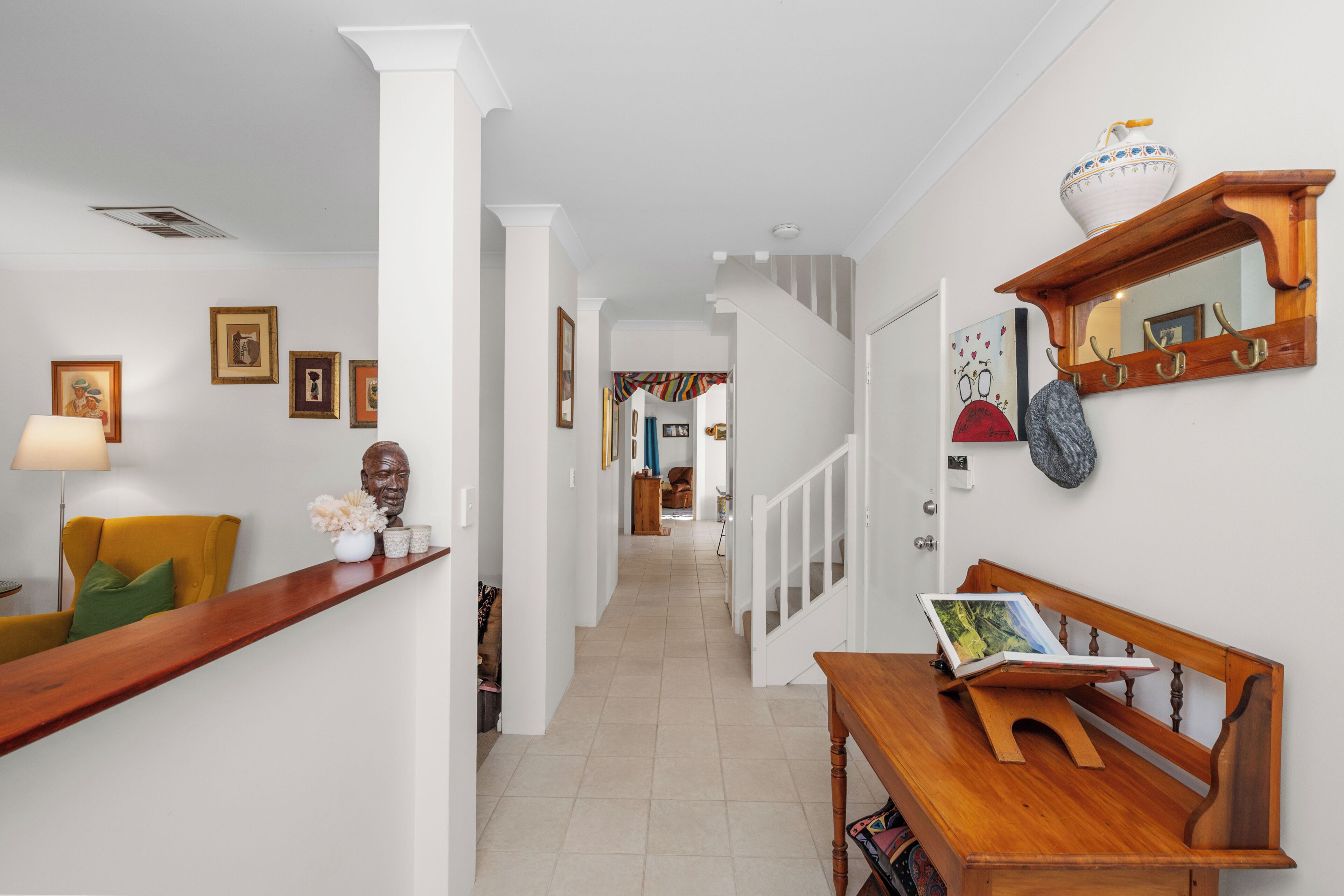 A hallway with a wooden bench, a lamp, and framed artwork on the walls.