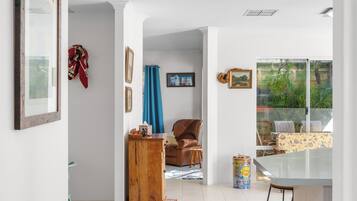A spacious room with a tiled floor, a wooden cabinet, a brown leather chair, a dining table with chairs, and a window with a view of greenery.