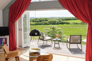 A balcony with a glass door, a TV, and a seating area with chairs and a table. - Outstanding contemporary country house, close to Bath with stunning views. (Bath)