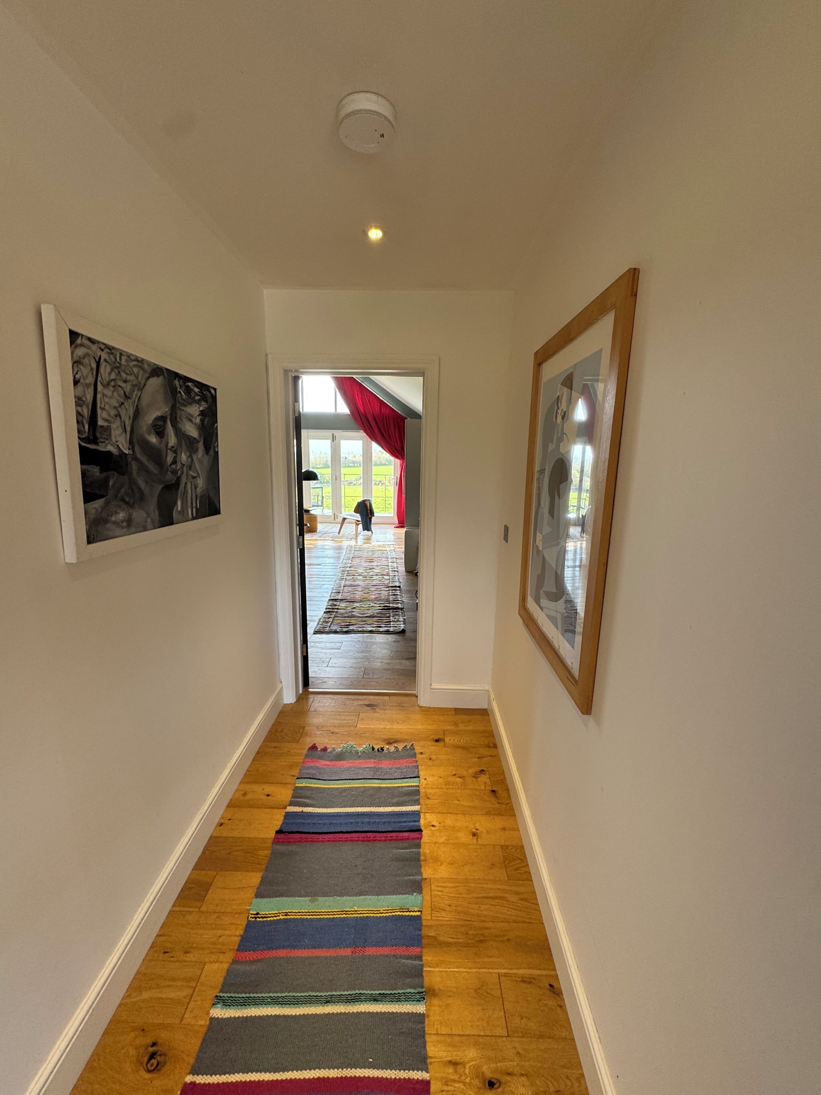 A hallway with a wooden floor, a colorful striped rug, and framed artwork on the walls.
