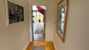 A hallway with a wooden floor, a colorful striped rug, and framed artwork on the walls.