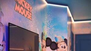Een televisie aan de wand, met een muurschildering van Mickey Mouse op de achtergrond.