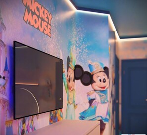 Ein an der Wand befestigter Fernseher mit einer Wandmalerei von Mickey Mouse im Hintergrund.