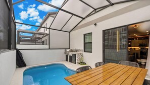 Ein Swimmingpool mit Holztisch und -stühlen, einem Grill und Blick zum Himmel.