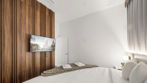 Ett hotellrum med en säng, en tv som är monterad på en väggpanel av trä och en dörr.