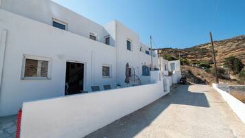 Un edificio blanco con numerosas ventanas y puertas, un sendero de concreto y un paisaje montañoso al fondo.