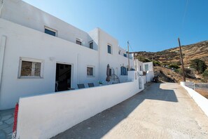 A white building with multiple windows and doors, a concrete pathway, and a hilly landscape in the background.