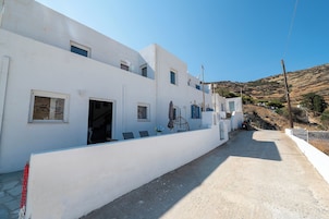 Un edificio blanco con numerosas ventanas y puertas, un sendero de concreto y un paisaje montañoso al fondo.