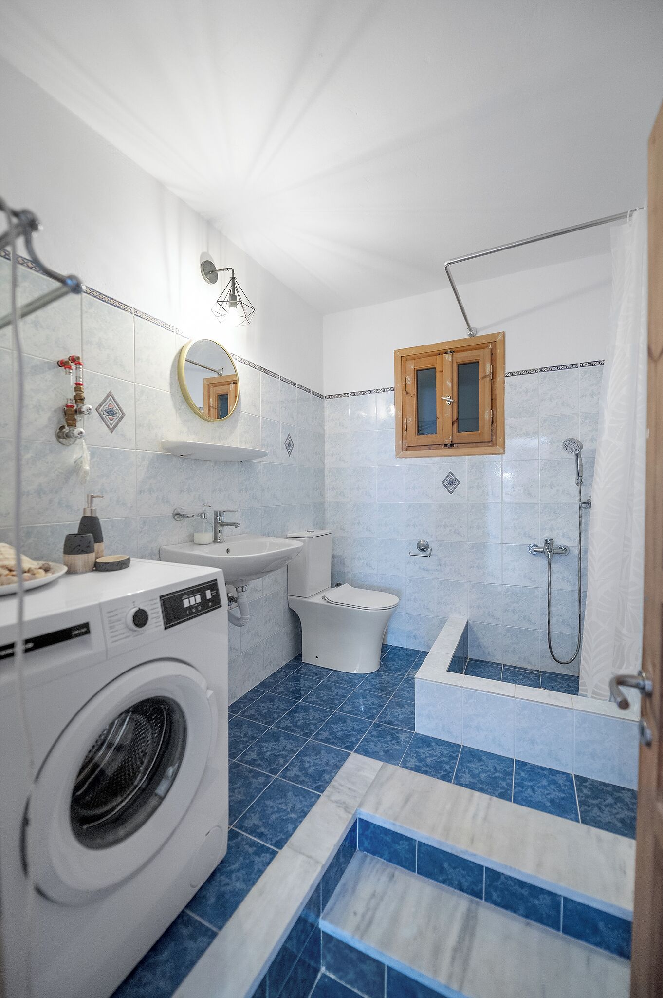 Un baño moderno con lavadora, lavabo, inodoro y zona de ducha.