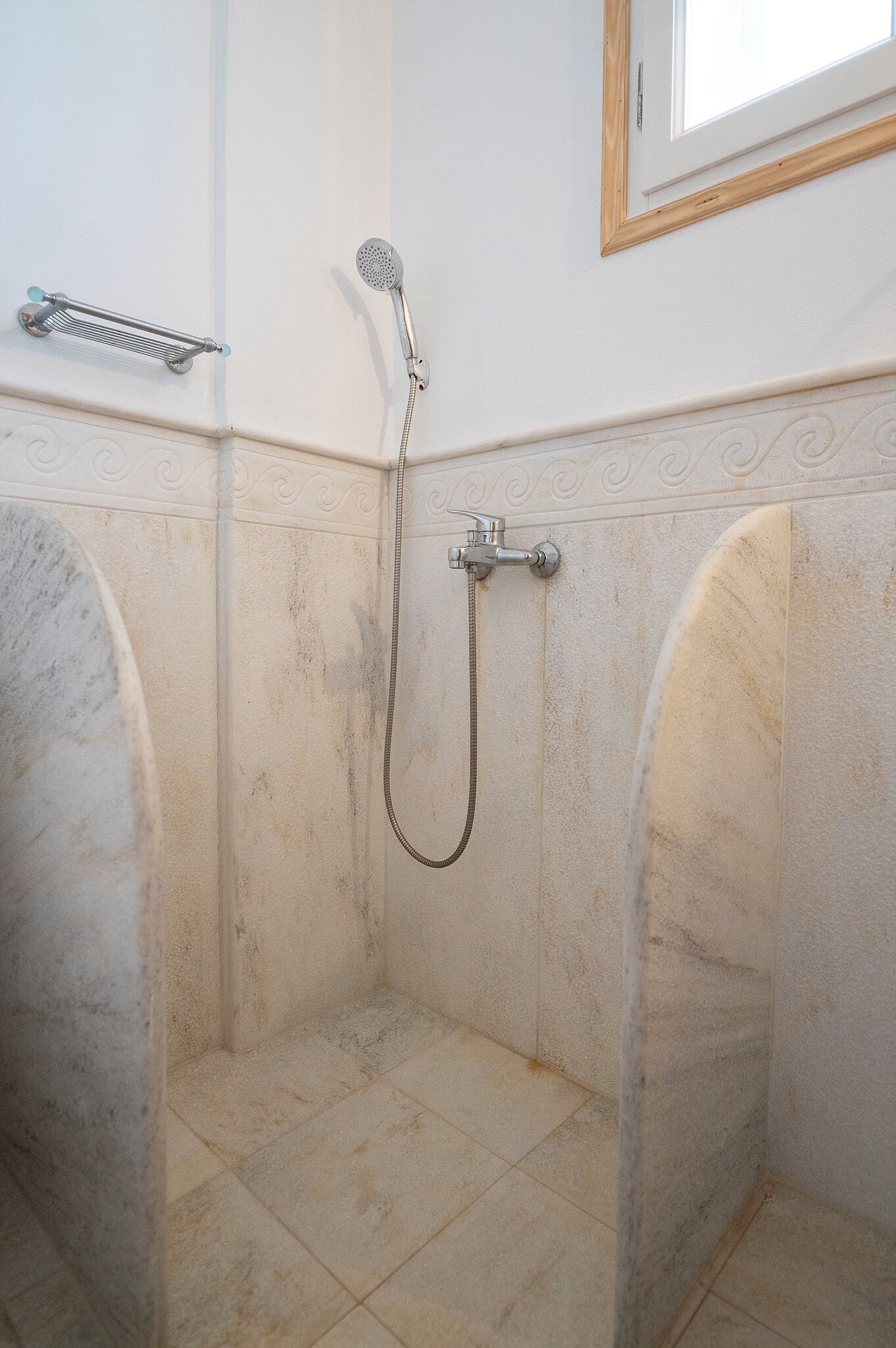 A bathroom with a shower, a towel rack, and a window.