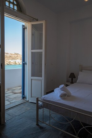 Un dormitorio con cama, mesita de noche, lámpara y vista al mar a través de una puerta abierta.