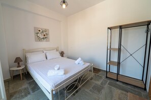 Un dormitorio con cama, mesita de noche con lámpara, un cuadro colgado en la pared y un armario con puerta espejada.