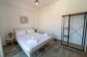 Un dormitorio con cama, mesita de noche con lámpara, un cuadro colgado en la pared y un armario con puerta espejada.