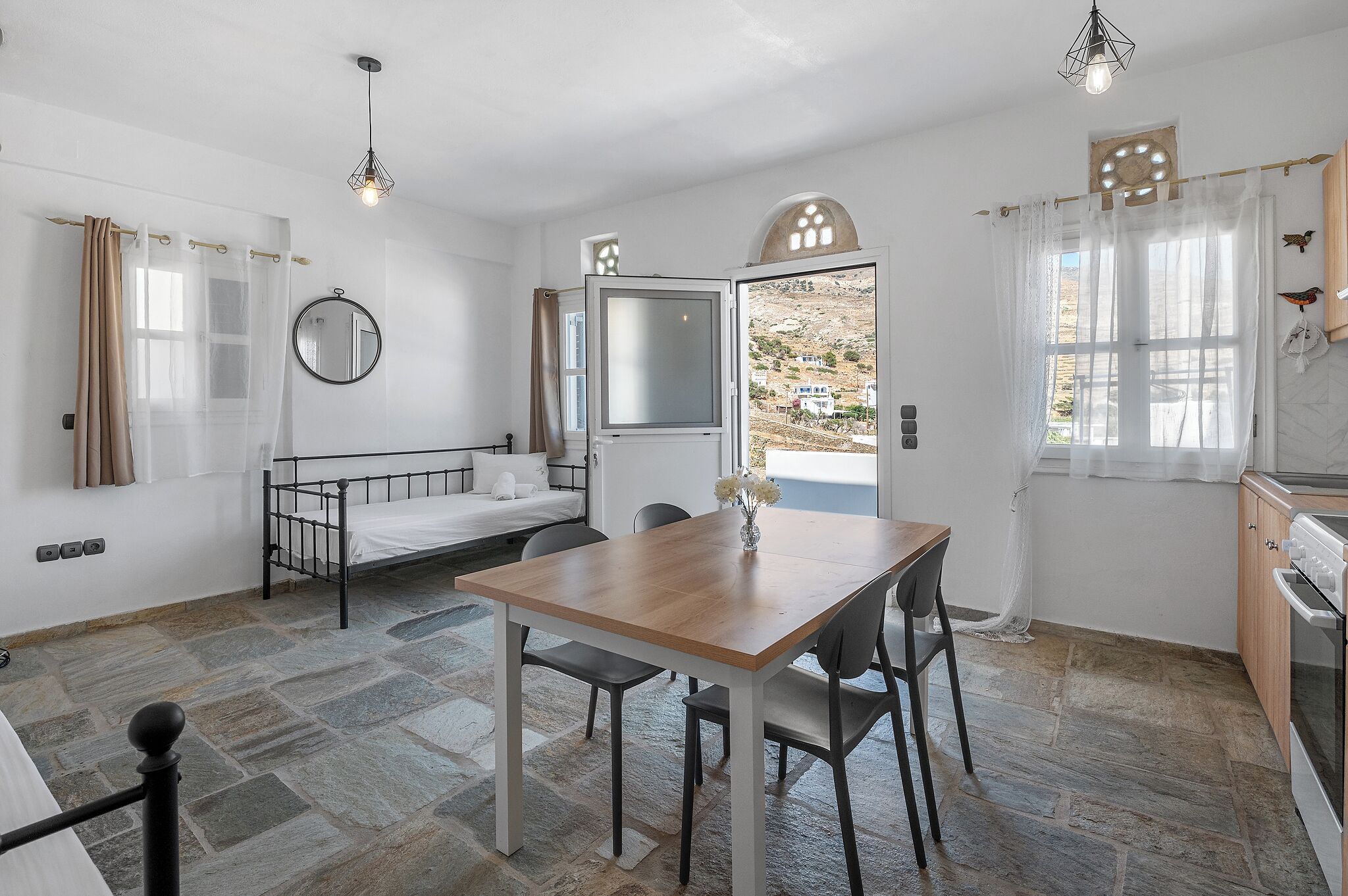 Ein Zimmer mit Bett, Esstisch mit Stühlen, Küchenzeile und Blick ins Freie.