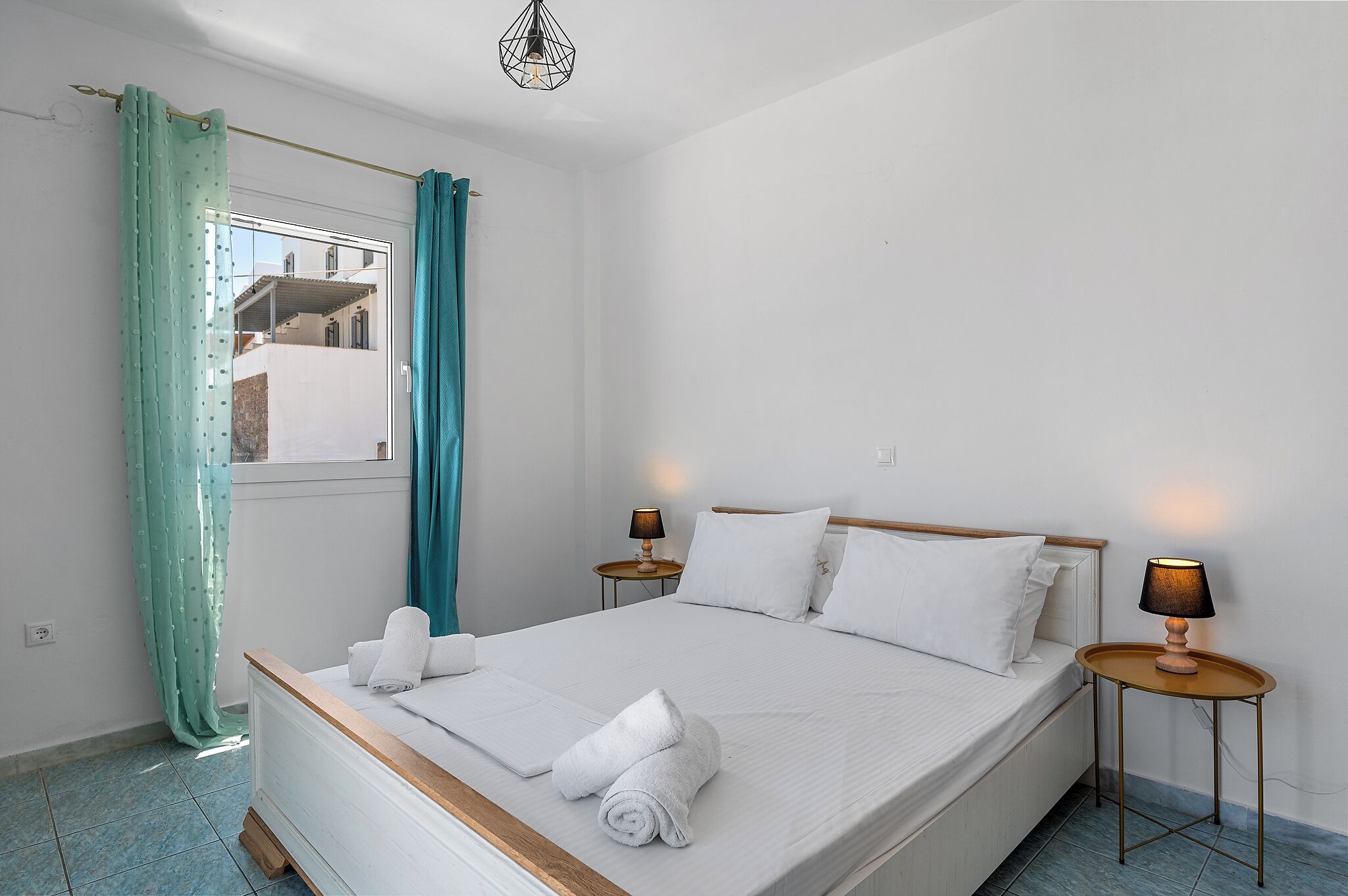 Un dormitorio con cama, dos lámparas de noche, una ventana con cortinas y vistas a edificios.