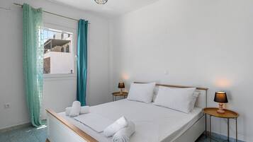 Un dormitorio con cama, dos lámparas de noche, una ventana con cortinas y vistas a edificios.