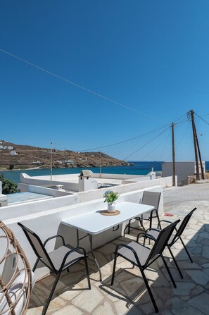 Un espacio de estar al aire libre con una mesa y sillas, con vista a un paisaje costero.