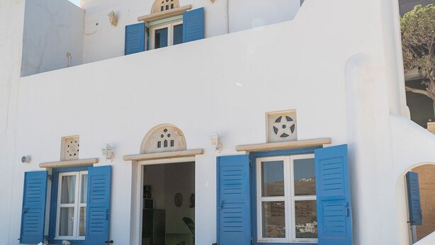 Un edificio blanco con contraventanas azules y una escalera de piedra que lleva a la entrada.