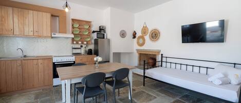 A compact kitchen with wooden cabinets, a dining table with chairs, a built-in oven, and a flat-screen TV mounted on the wall.