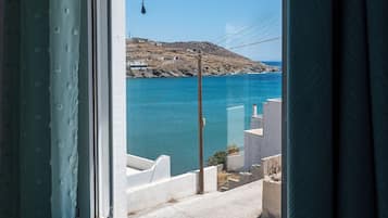 Una ventana con vistas a un paisaje costero, que incluye una masa de agua y una zona montañosa con edificios.