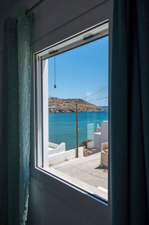 Una ventana con vistas a un paisaje costero, que incluye una masa de agua y una zona montañosa con edificios.