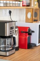 Una cocina con cafetera, un electrodoméstico rojo y una tetera sobre la encimera.
