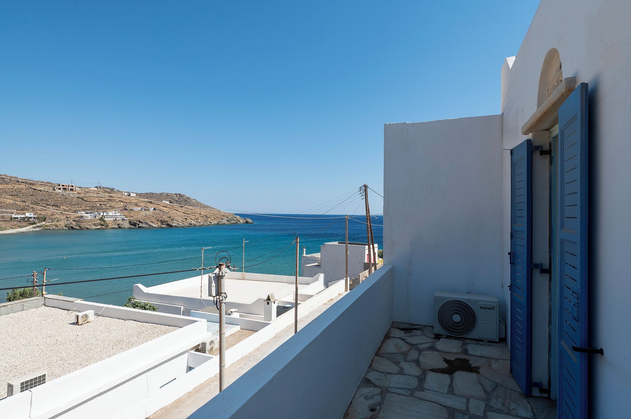 Un balcón con vista al mar y un edificio blanco con contraventanas azules.