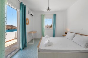 A hotel room with a bed, a small desk, a window with curtains, and a view of the sea.