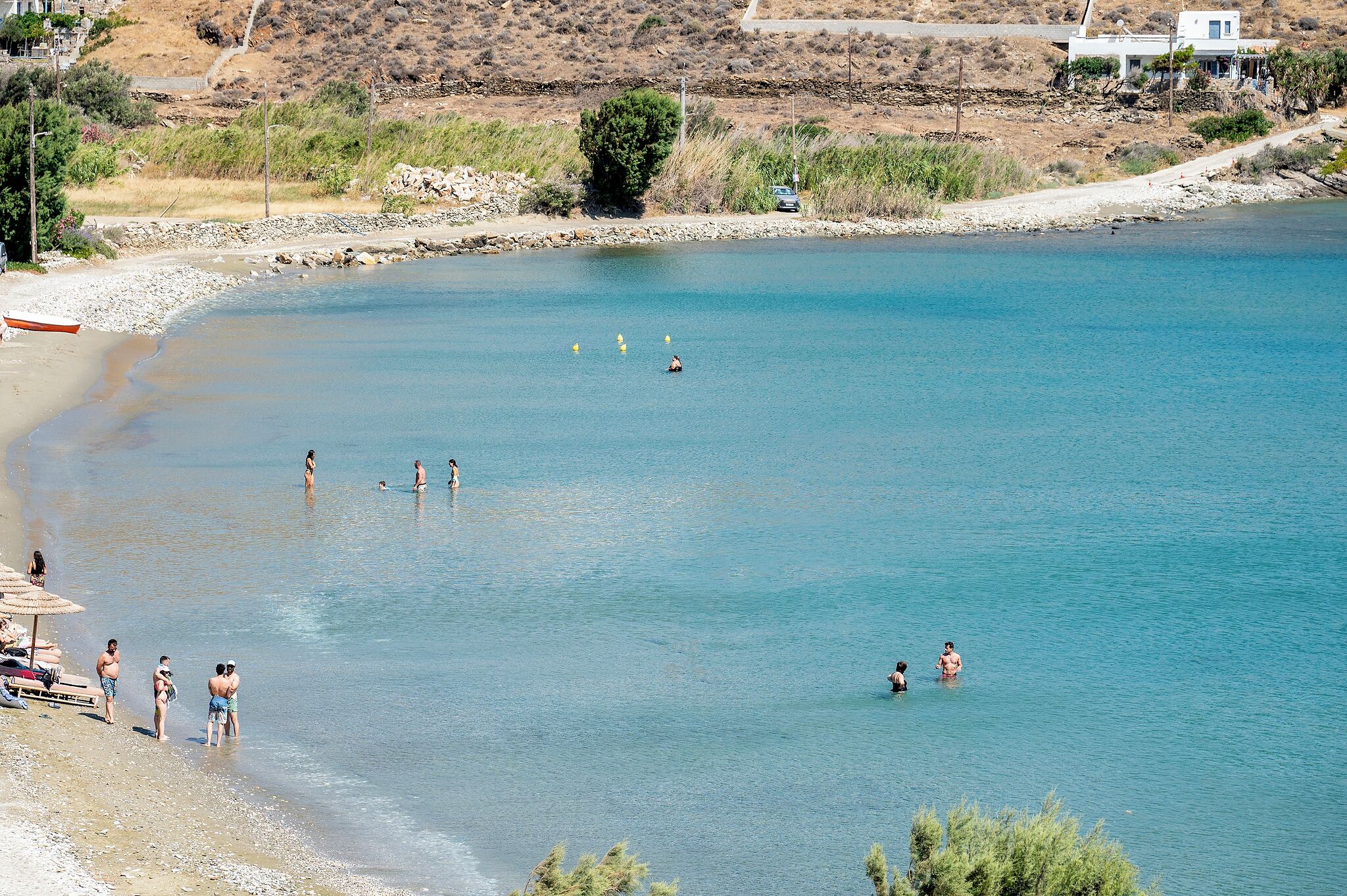 Una playa con agua cristalina, gente nadando y un bote en la orilla.