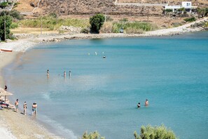 A beach with clear water, people swimming, and a boat on the shore. - Seafront maisonettes by TinosStay (Kardiani)