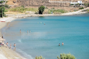 Egy tiszta vizű strand, ahol emberek úszkálnak, és egy csónak horgonyzik a partján.